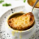 white bowl full of french onion soup topped with melted cheese and crisp french baguette