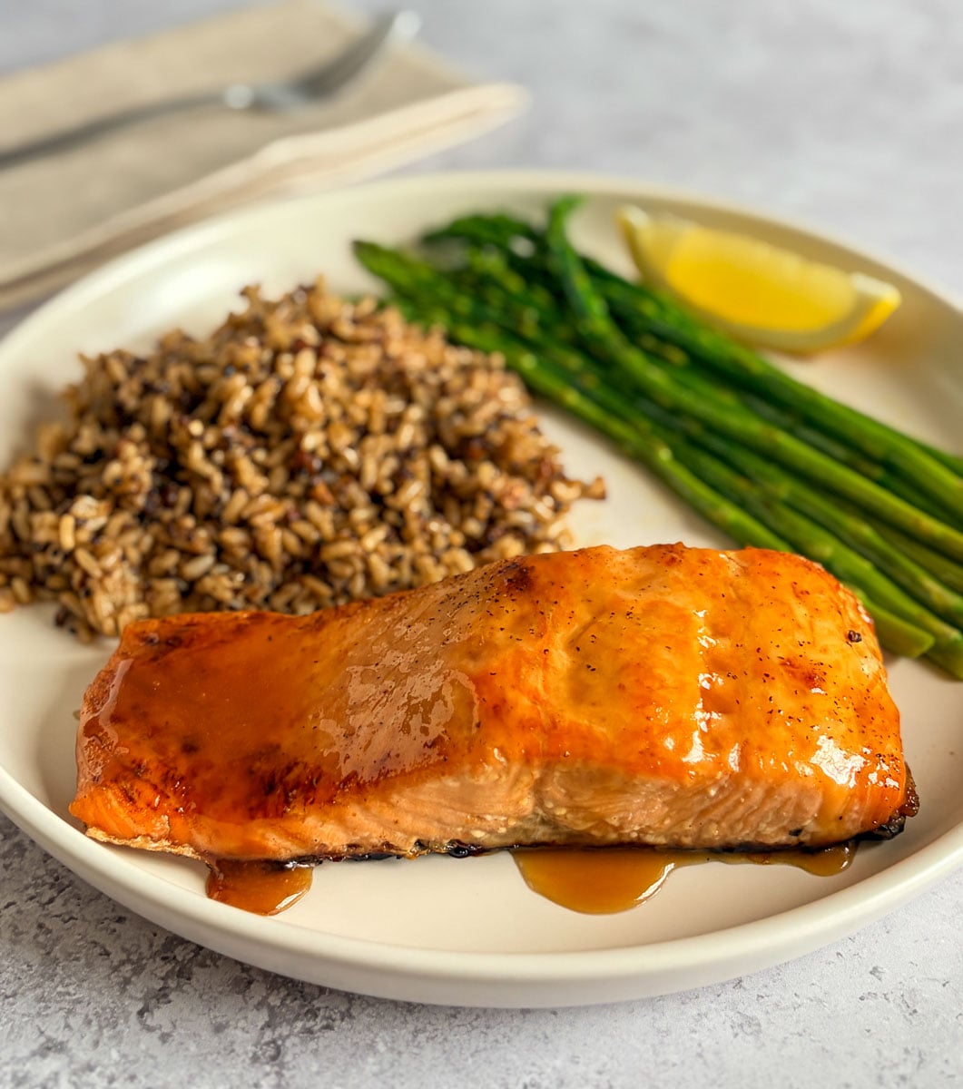maple brown sugar glazed salmon fillet on a plate with rice, asparagus, and lemon wedge