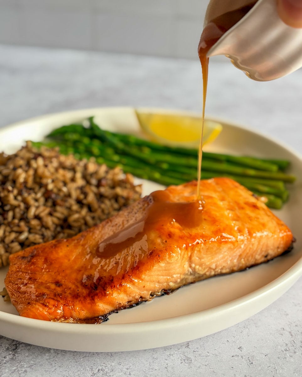 maple brown sugar glaze drizzled over salmon filet on a plate with rice and asparagus