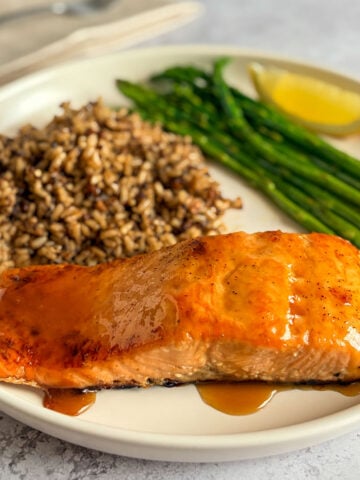 Maple brown sugar glazed salmon on a plate with rice, asparagus, and lemon wedge