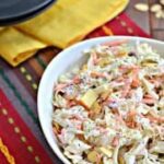 white bowl of coleslaw with apples, cranberries and almonds on festive placemat