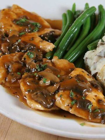 plate of chicken marsala topped with mushrooms, red skinned mashed potatoes and green beans