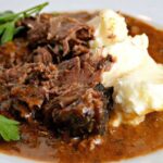 white plate with slow cooker pot roast, gravy and mashed potatoes