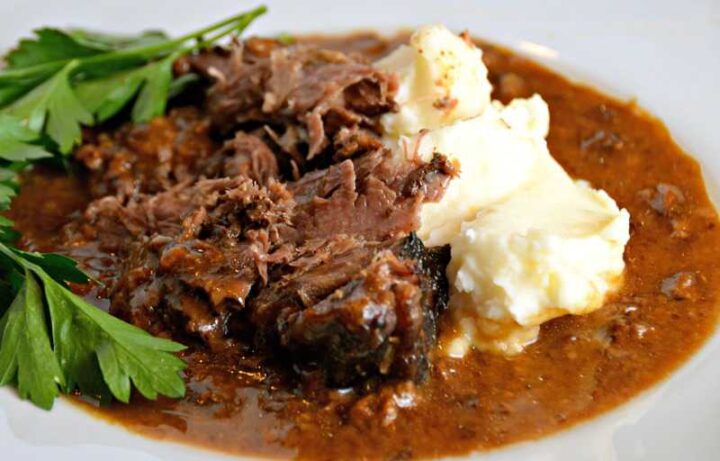 white plate with slow cooker pot roast, gravy and mashed potatoes