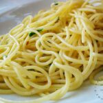 white plate with fluffy spagetti aglio e olio, red pepper flakes and parsely
