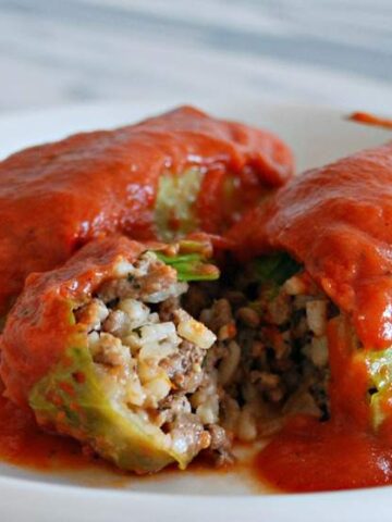 stuffed cabbage leaves with ground beef and rice topped with tomato based sauce on a plate
