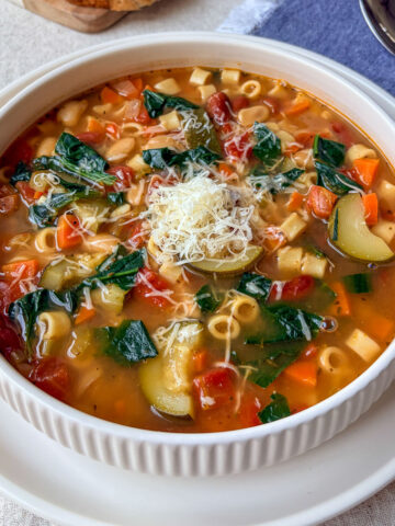 bowl of minestrone soup on table with spoon and bread