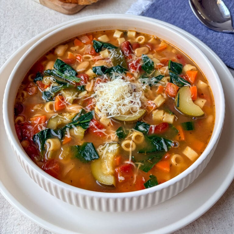 bowl of minestrone soup on table with spoon and bread