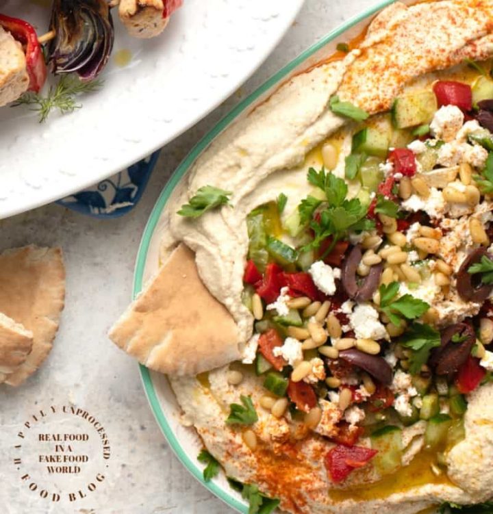 LAYERED HUMMUS DIP - Homemeade Hummus topped with Kalamata olives, cucumbers, roasted red peppers, feta cheese and pine nuts #hummus #healthy #chickpeas #tahini #happilyunprocessed