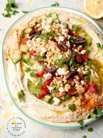 LAYERED HUMMUS DIP - Homemeade Hummus topped with Kalamata olives, cucumbers, roasted red peppers, feta cheese and pine nuts #hummus #healthy #chickpeas #tahini #happilyunprocessed