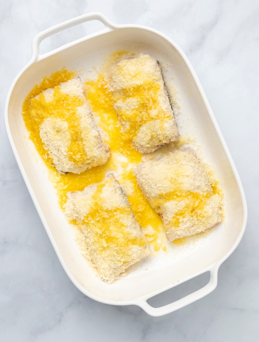 Pieces of cod in a baking dish with Panko breadcrumbs on top drizzled in butter waiting to be baked