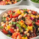 Summer four bean salad with black beans, kidney beans, cannellini beans, chickpeas, tomatoes, peppers, olives, red onion, and fresh herbs.