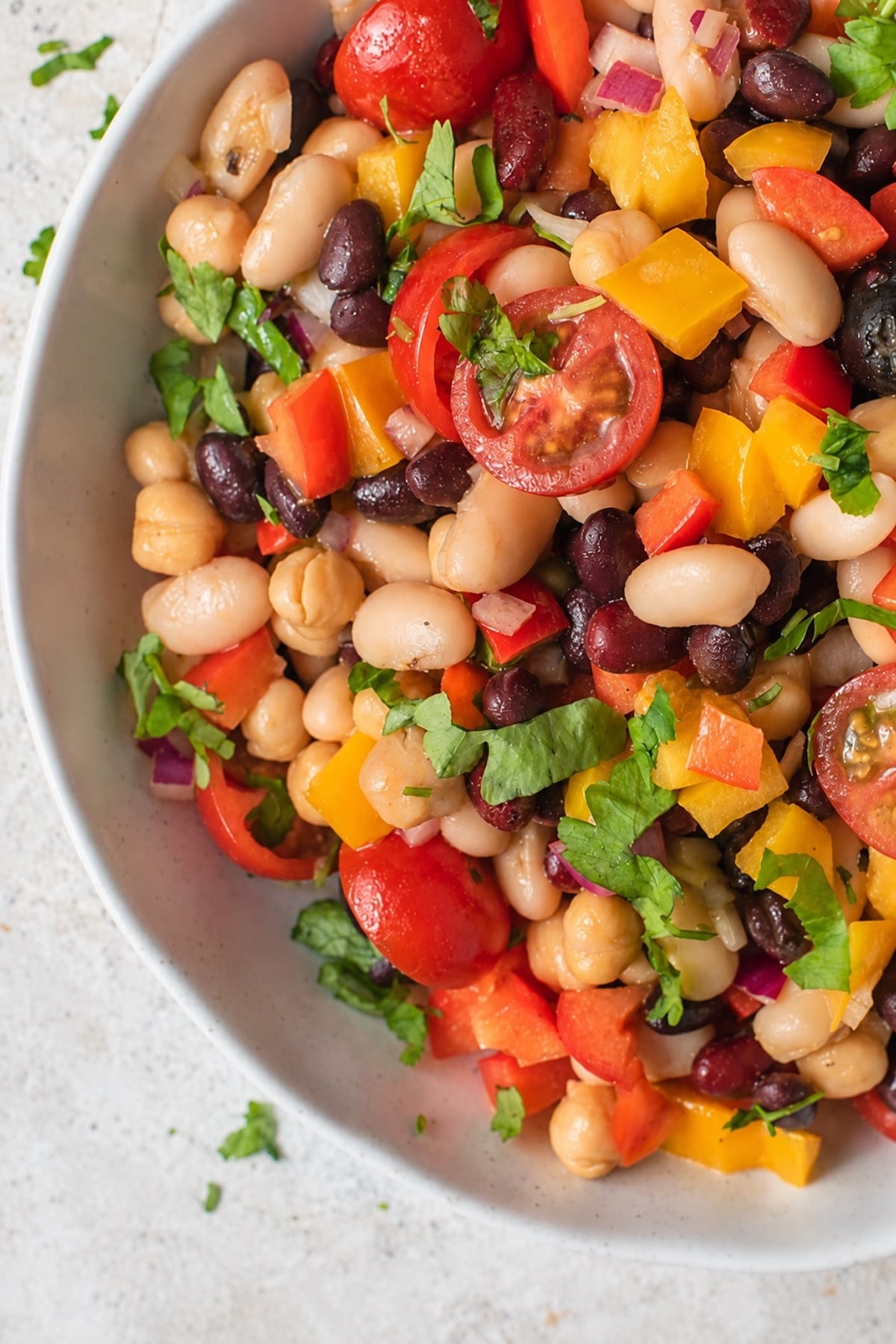 Summer four bean salad with black beans, kidney beans, cannellini beans, chickpeas, tomatoes, peppers, olives, red onion, and fresh herbs.
