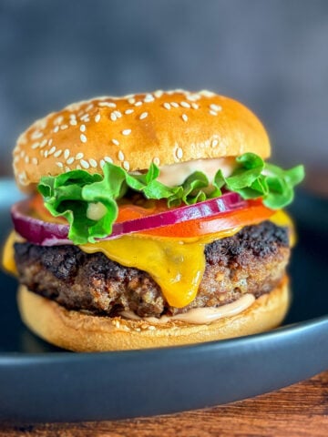 juiciest burger on a plate topped with lettuce, onion, tomato, cheese, and burger sauce
