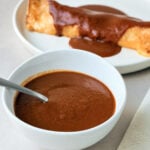 white bowl of homemade red enchilada sauce and enchilada covered in sauce