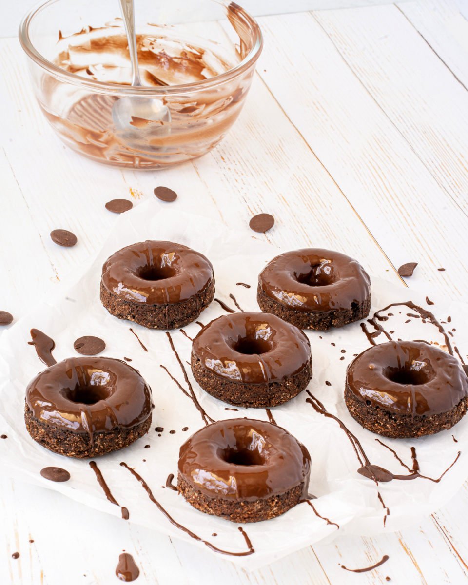 Almond flour chocolate donuts spread out on a table topped with homemade chocolate drizzle sauce.