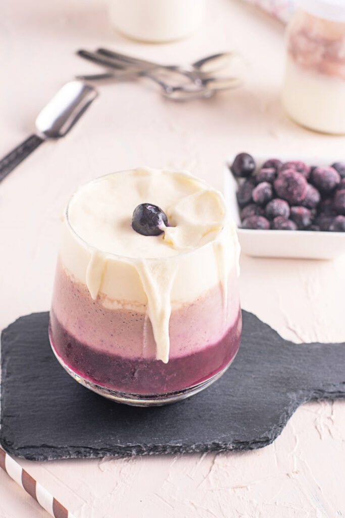A healthy triple layered blueberry and banana smoothie topped with fresh whipped cream in a glass