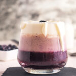 A healthy triple layered blueberry and banana smoothie topped with fresh whipped cream in a glass