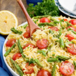 Lemon Orzo with tomatoes and asparagus with a wooden spoon in a large bowl