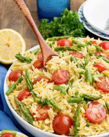 Lemon Orzo with tomatoes and asparagus with a wooden spoon in a large bowl