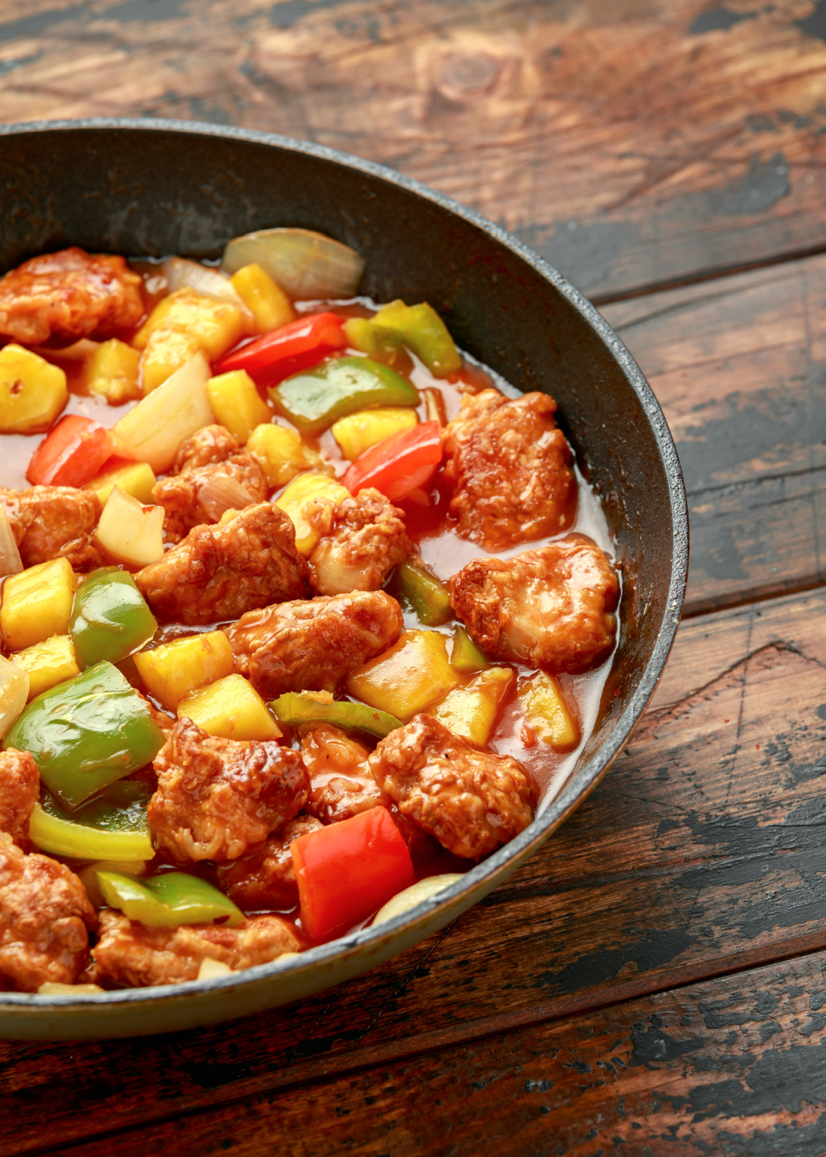 Sweet and sour chicken in a pan with pineapple and peppers
