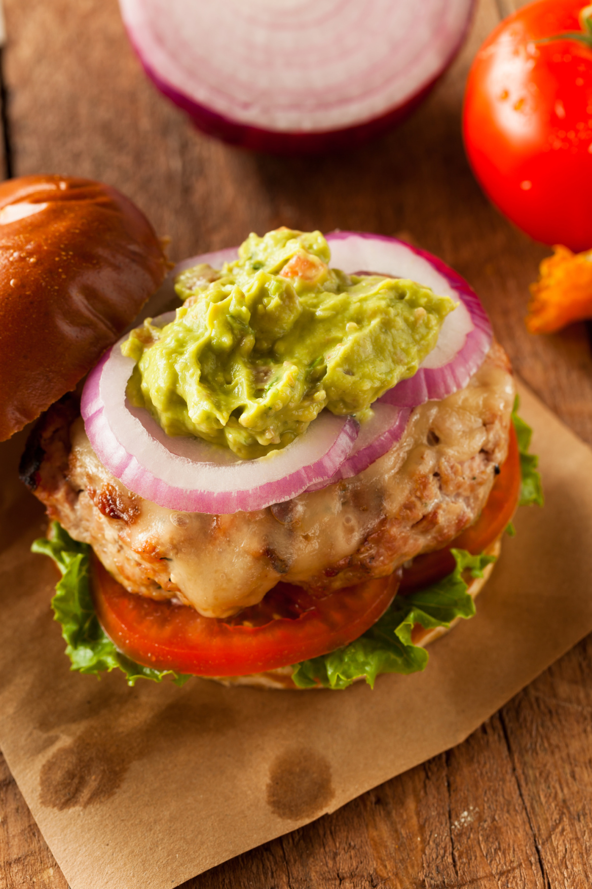 A delicious juicy homemade turkey burger with Gruyere cheese on a bun topped with sliced onion and guacamole