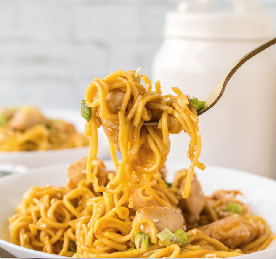 A big bite full of garlic and ginger chicken and chow mein noodles garnished with scallions.