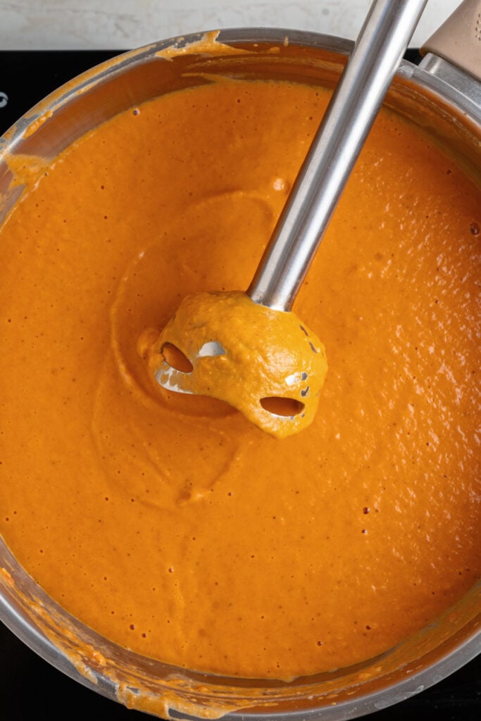 close up of immersion blender blending chicken makhani (butter chicken) sauce