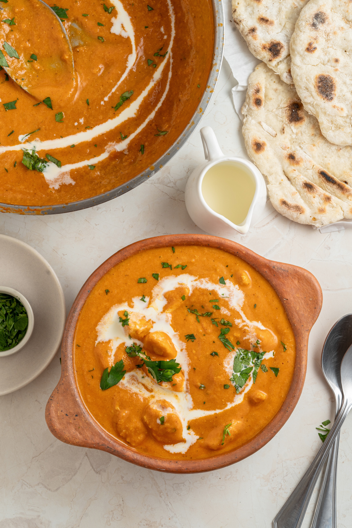 a bowl of buttery, spicy Indian Chicken Makhali with a splash of cream and naan bread