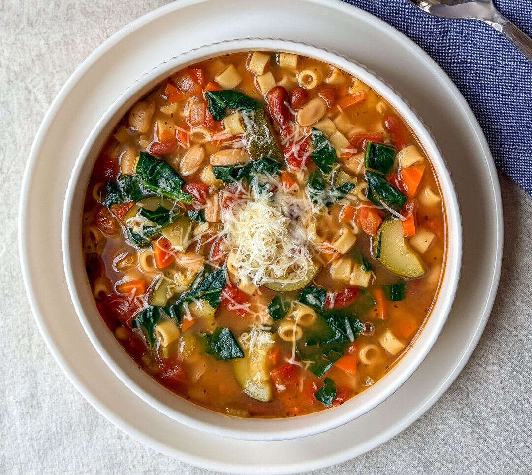 a bowl of minestrone soup on a table with spoon and bread
